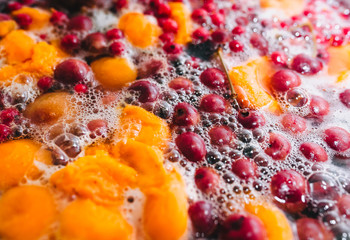Fototapeta na wymiar Fresh fruits: apricots, cherries, raspberries, apples are boiled in boiling water in a metal pan on a stove with bubbles and foam close-up. Cooking delicious homemade compote. Photography, concept.