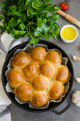 Traditional Ukrainian garlic bread buns in a cast-iron frying pan on a dark concrete background. Vertical orientation, top view, copy space.