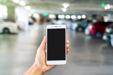 Woman hand holding smart phone with blank screen in blur department store car parking background, close up, copy space