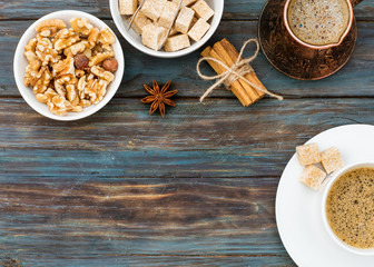 Cup of coffee, nuts in the bowl, coffeepot, cinnamon, anise, sugar, coffee beans on a wooden  background
 Lay with no people. View from the top.
