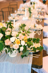 Vertical frame, top view. The focus is on the central floral arrangement, placed on fabric, covering the festive table, beautifully served with sets of dishes and glasses.