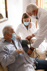 Anziano con mascherina viene visitato da un medico a casa che gli prende la pressione sanguigna...