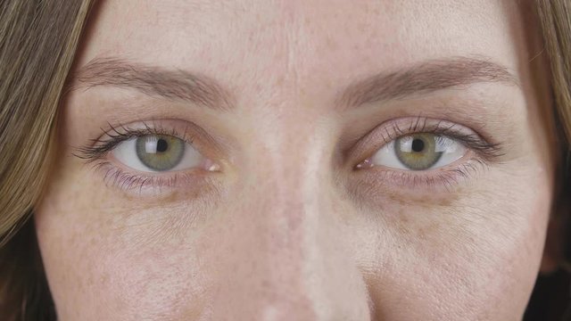close-up portrait freckled face of light brown haired woman with green eyes blink slow. 4k