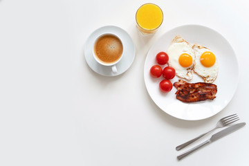 Classic breakfast with two eggs, bacon, fresh tomatoes, black coffee and fresh orange juice on the white table. Copy space. Top view.