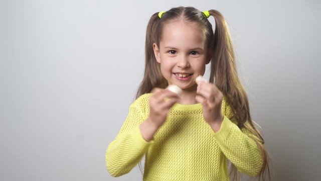Joyful girl eating meringues on a stick in a yellow sweater on a white background