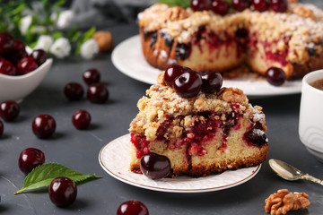 Homemade cherry pie with shtreisel and walnuts on white plate on a dark concrete background, piece of cake is located in the foreground, horizontal format