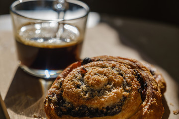 Glass cup of coffee and saucer with a cinnamon roll. Sweet breakfast.