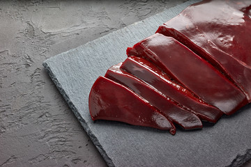Fresh raw beef livers on a black stone cutting board  on dark background.