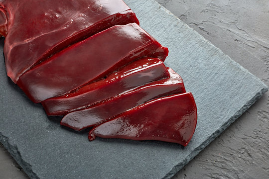 Fresh raw beef livers on a black stone cutting board  on dark background.