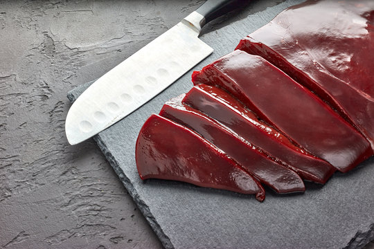 Fresh Raw Beef Livers On A Black Stone Cutting Board  On Dark Background.