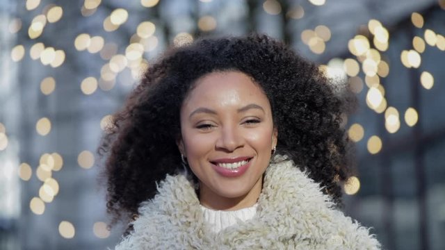 Confident african american woman is posing with toothy smile, standing outdoors on spring day spbi. Young attractive female is looking forward with positive emotions while having time on street with