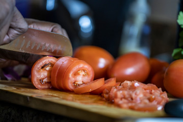 close up view African american woman hand cutting tomatoes into thin slices for healthy and nutritious meal lifestyle. the organic meal the culinary chef is making is delicious