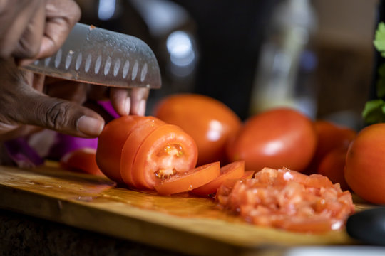 close up view African american woman hand cutting tomatoes into thin slices for healthy and nutritious meal lifestyle. the organic meal the culinary chef is making is delicious