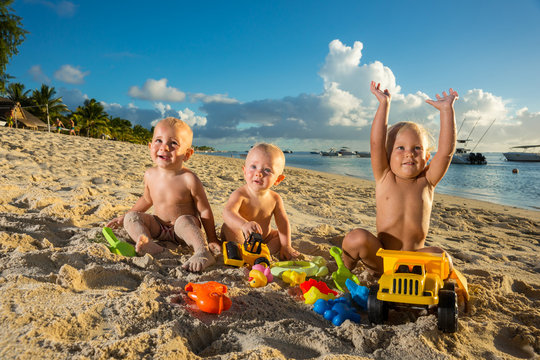 babies play with toys on the sand against the background of the transparent ocean and snow-white yachts