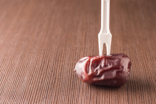 Single date fruit on a wooden table with a stuck fork