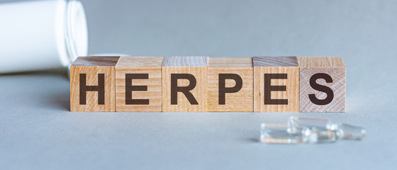 Herpes - word text from wooden cube blocks with letters, viral diseases herpes viruses concept. Cube blocks with scattered ampoules on grey background.