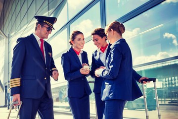 Portrait of mature pilot talking with young attractive flight attendants during arrival in airport
