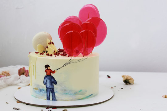 White cream cake with a picture of dad and daughter, decorated with lollipops on sticks on the cake stand.