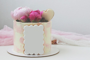 Pink cream cake with peonies and gingerbread in the shape of a heart. A birthday present. Selective focus.