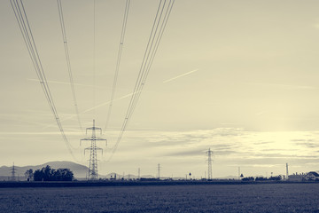 Power transimission lines running across fields at sunset.