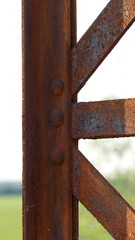 An old disused rusted brown bridge in the countryside connecting two banks across a river, formerly used for busy agricultural traffic