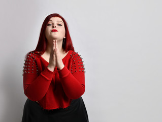 Overweight redhead woman in red spiked top, black leather skirt. She has folded palms and begging...