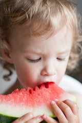 Little curly girl with pleasure eats a slice of watermelon in the summer