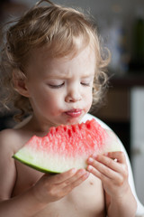 Little curly girl with pleasure eats a slice of watermelon in the summer