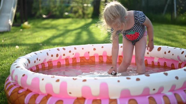 little girl playing in inflatable kiddie pool outside in backyard in summertime