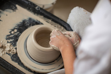The hands of a professional who creates a pot of clay on a potter's wheel. Close-up, top view. Pottery workshop, process of work.