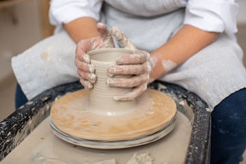 The potter's hands forming pottery from clay on a potter's wheel. Craft production. 