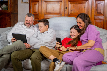 Happy family sitting on sofa and using digital tablet and mobile phone at home - Father and son...