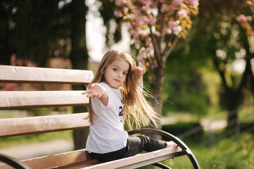 Happy female kid sits on the bench in the park. Fresh air. End of quarantine