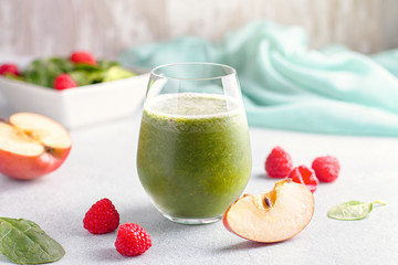 Glass of green smoothie with spinach, raspberry and apple on concrete table, still life. Healthy freshly blended fruits and herbs smoothie with wooden background