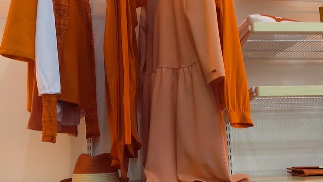 Clothing in orange hangs on hangers in a closet. Folded clothes on shelves