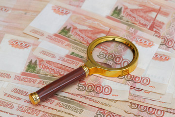 A magnifying glass with a gold handle is placed on top of Russian banknotes of five thousand rubles in large quantities