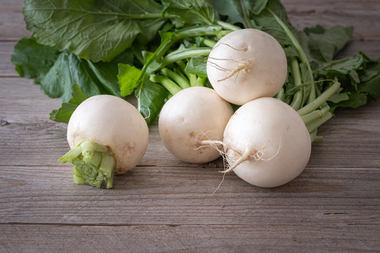 Bunch of white turnips on wooden background. Front view of fresh spring vegetable with green leaves
