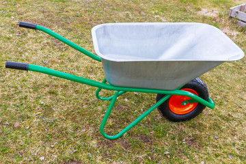 Garden metal wheelbarrow with green reinforced frame on one wheel in the garden - 349969748