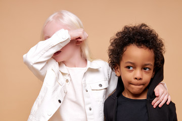 portrait of black afro and albino kids at a loss, girl with unusual appearance closed her eyes with...