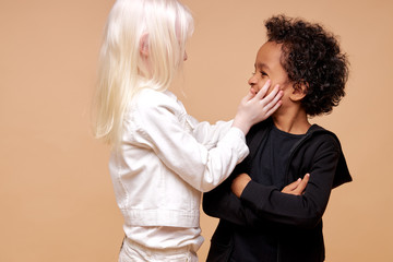 sensitive albino child girl touch face of multiracial boy isolated in studio. adorable girl with white hair has tender feelings for the boy