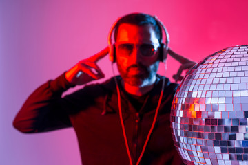 Colorful studio portrait of a bearded deejay with headphones and sunglasses against red and blues...