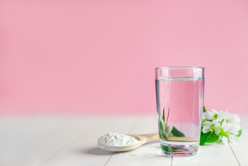 glass of water, spoon with collagen powder white flowers