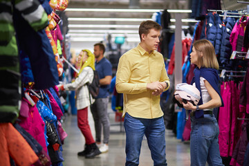 young beautiful caucasian couple came in sportive wear store, they lead healthy lifestyle, want to buy helmet and other wear for skiing