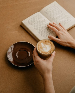 Book and coffee on a table with a woman's hands