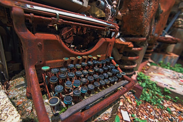 Classic rusty typewriter sits broken and discarded on ground exposed to elements a relic of previous times. Part of an art installation Cathedral of Junk in Austin.