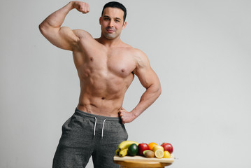 Sexy vegan guy with a naked torso posing in the Studio next to fruit. Diet. Healthy diet