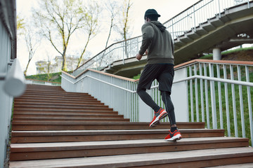 Staying healthy and fit. Full length of athletic dark skinned man in black sportswear running upstairs. Morning cardio. African man jogging in the city