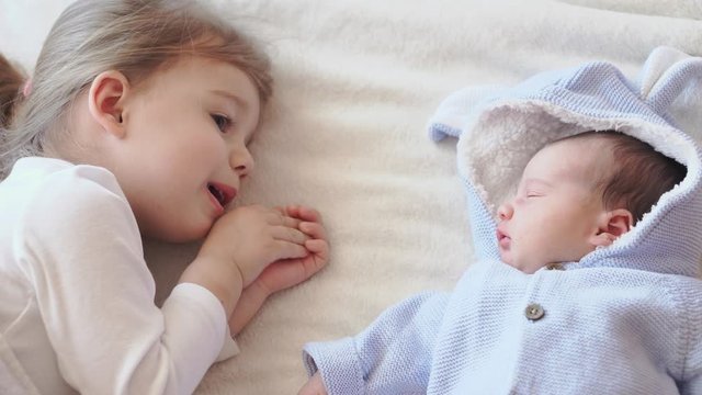 Childhood, infancy, family, sleep, rest concept - close up of two children, newborn baby and three year old girl sleeping together on a beige and white bed. Sisters are sleeping on the couch at home.