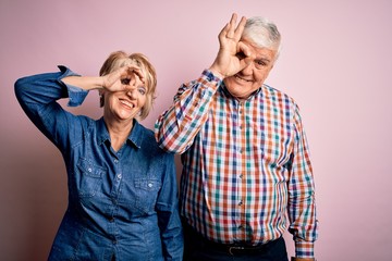 Senior beautiful couple standing together over isolated pink background doing ok gesture with hand smiling, eye looking through fingers with happy face.