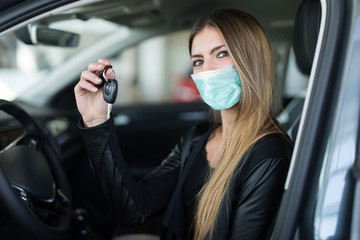 Masked woman showing the key of her new car in a car dealer saloon